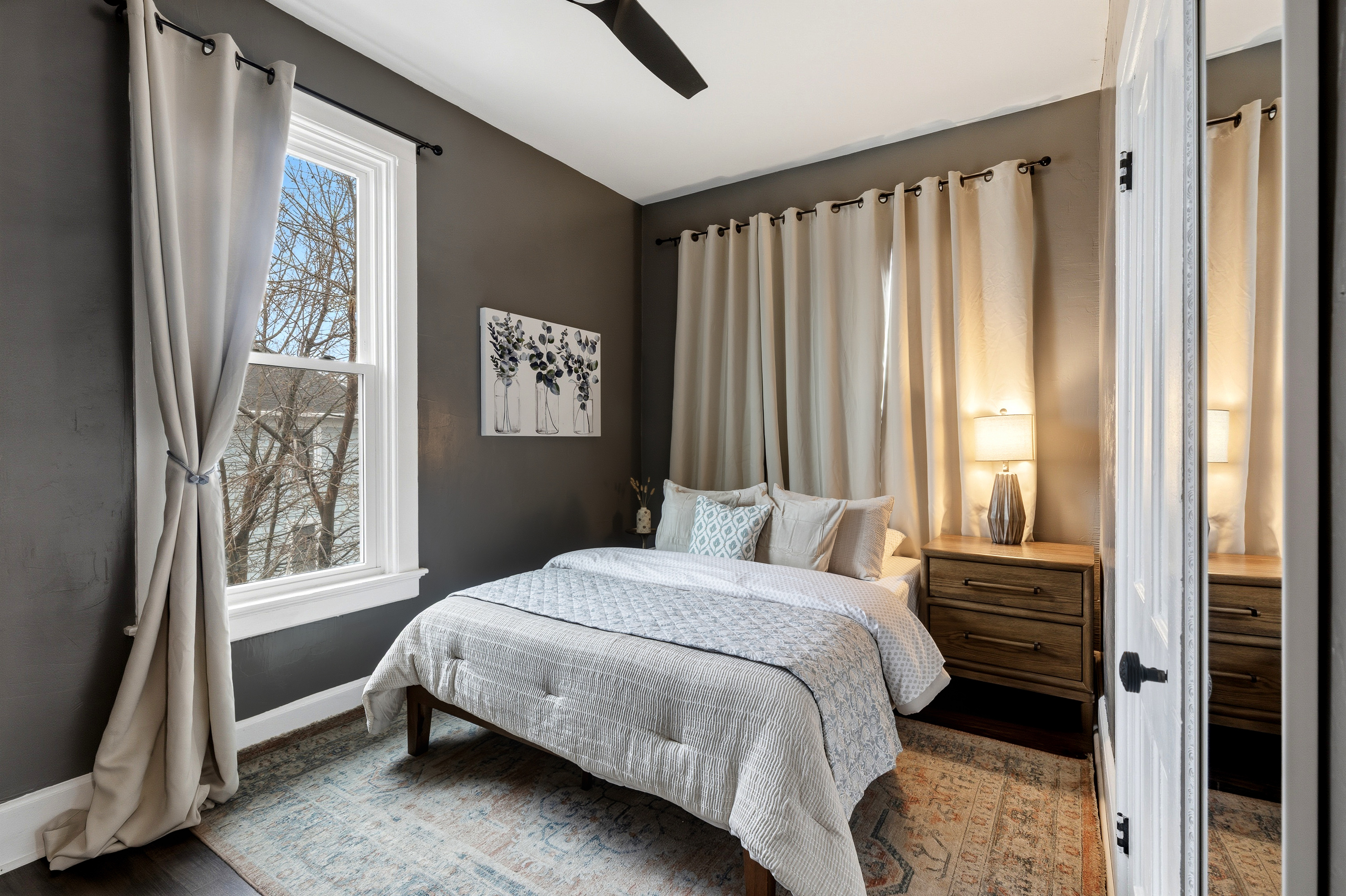 Bright and airy queen bedroom with natural light and calming neutral tones.  Features a ceiling fan, walk-in closet, smart TV, and full-length mirror.