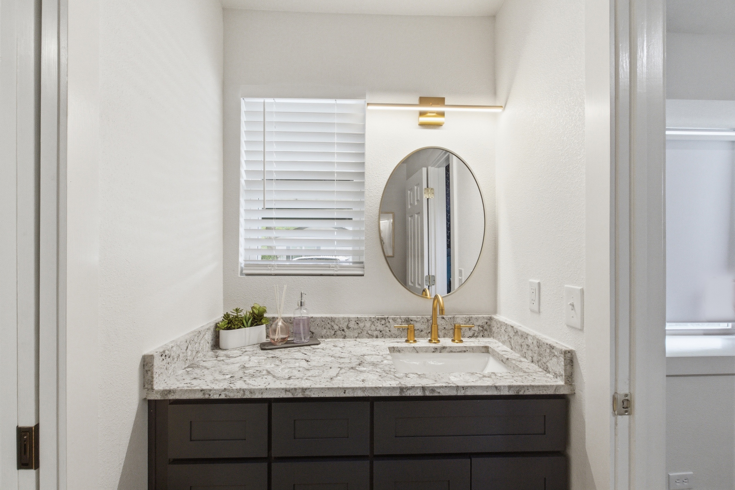 Dual vanity with round mirror, gold fixtures, and marble countertop. Stocked with Ginger Lily Farms bath essentials. One of 2.5 bathrooms in this 4-bedroom Arlington vacation rental.