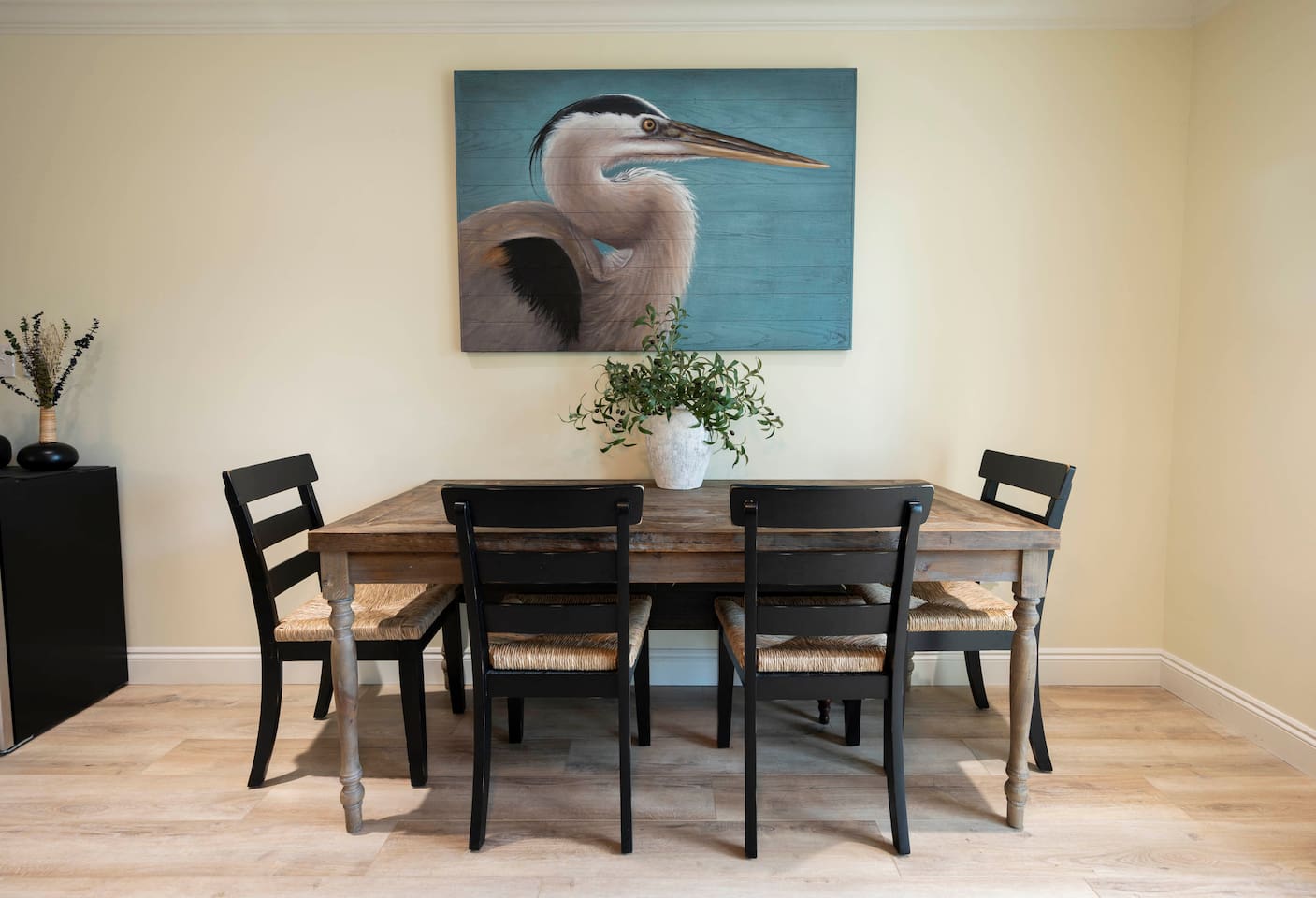 Rustic dining charm: Heron art, cozy table, and stylish black chairs.