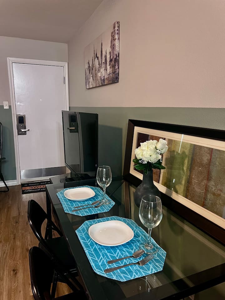 Dining corner with a small table, full-size fridge, TV, and an easy spot for meals or work.
