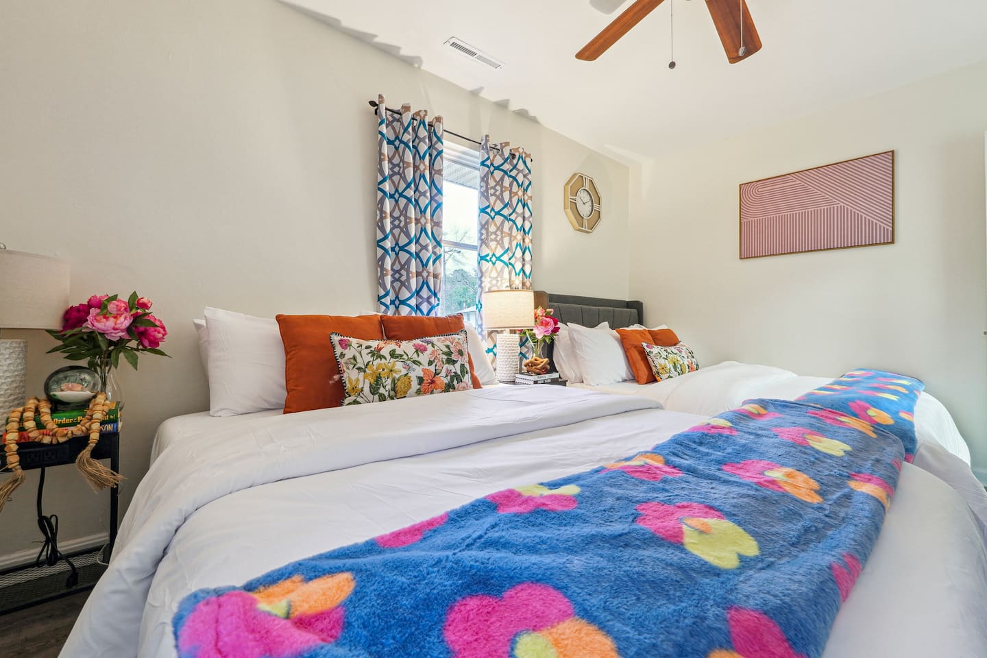 Step into a comfortable bedroom featuring two Queen beds, a ceiling fan, a TV, a clock, and a basket of fresh towels, providing everything you need for a relaxing and restful stay.


