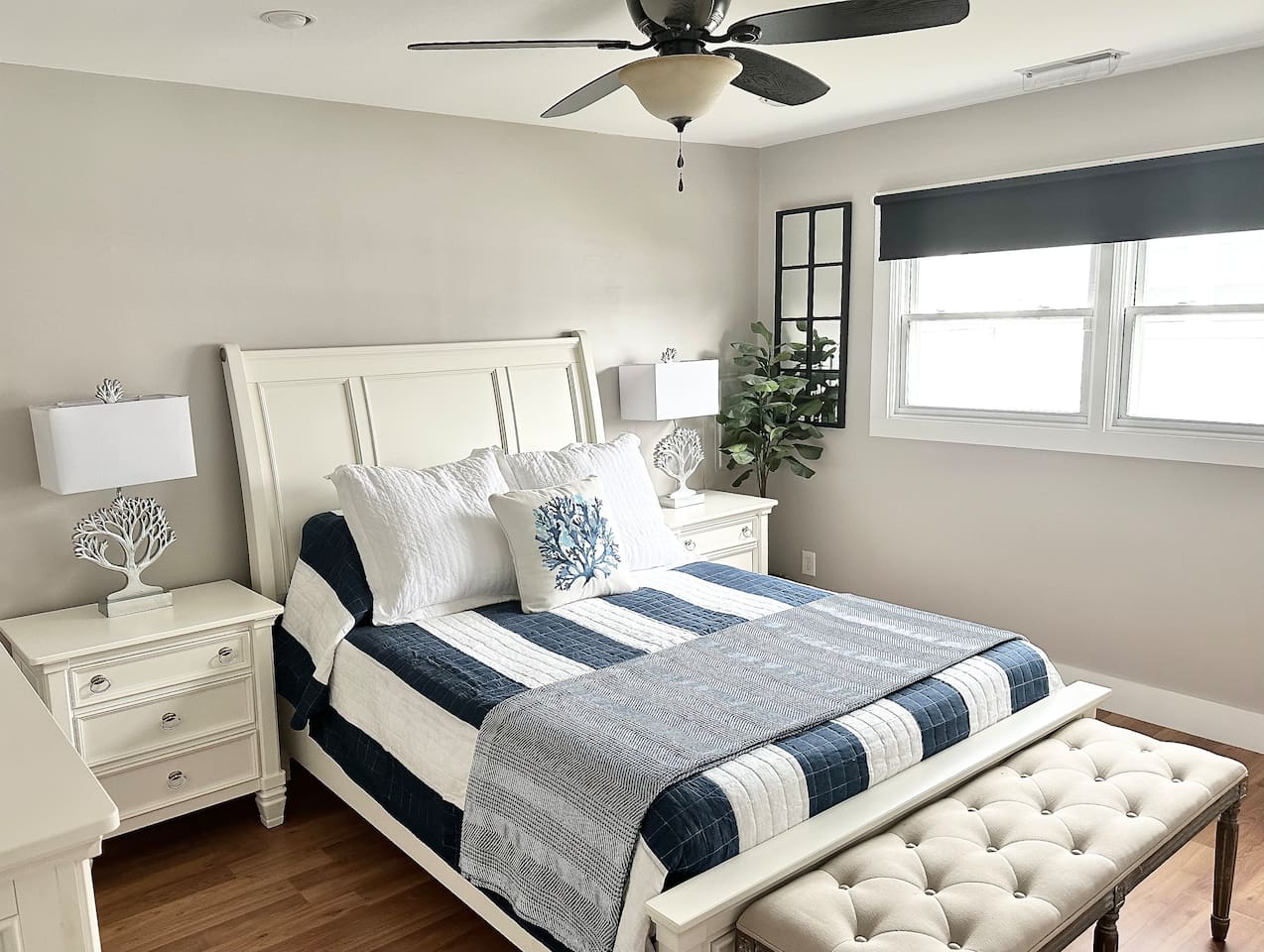 Rest easy in this bright bedroom featuring a white panel bed and matching nightstands. The space is accented by a tufted bench and coral-themed lamps, creating a serene, coastal atmosphere for a perfect night's sleep.