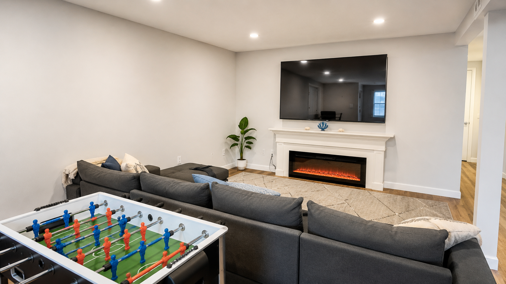 Basement living room with sectional, large smart TV, and electric fireplace