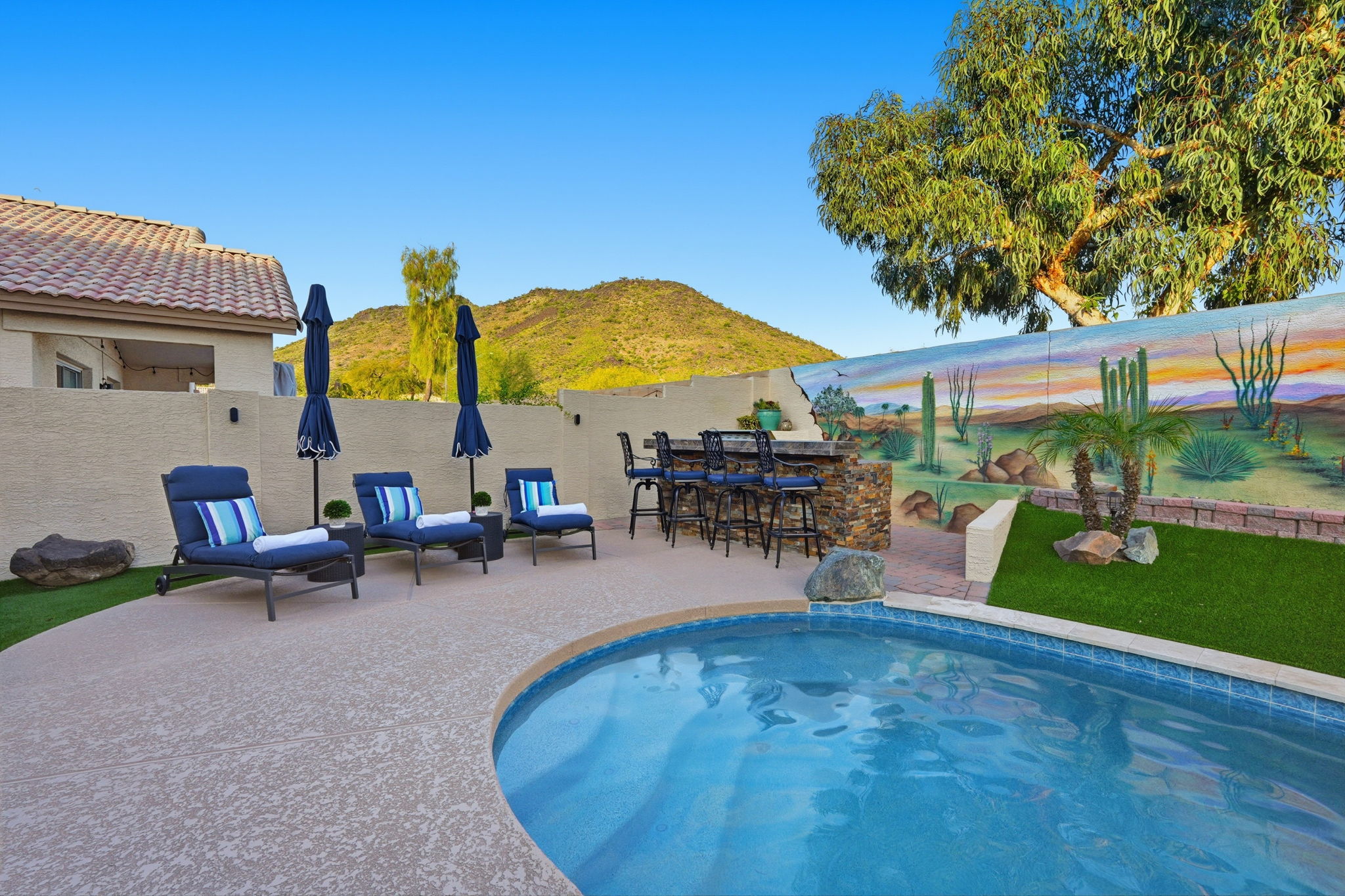 Private pool area with lounge seating, outdoor bar, desert mural, and mountain views for sunny backyard downtime.