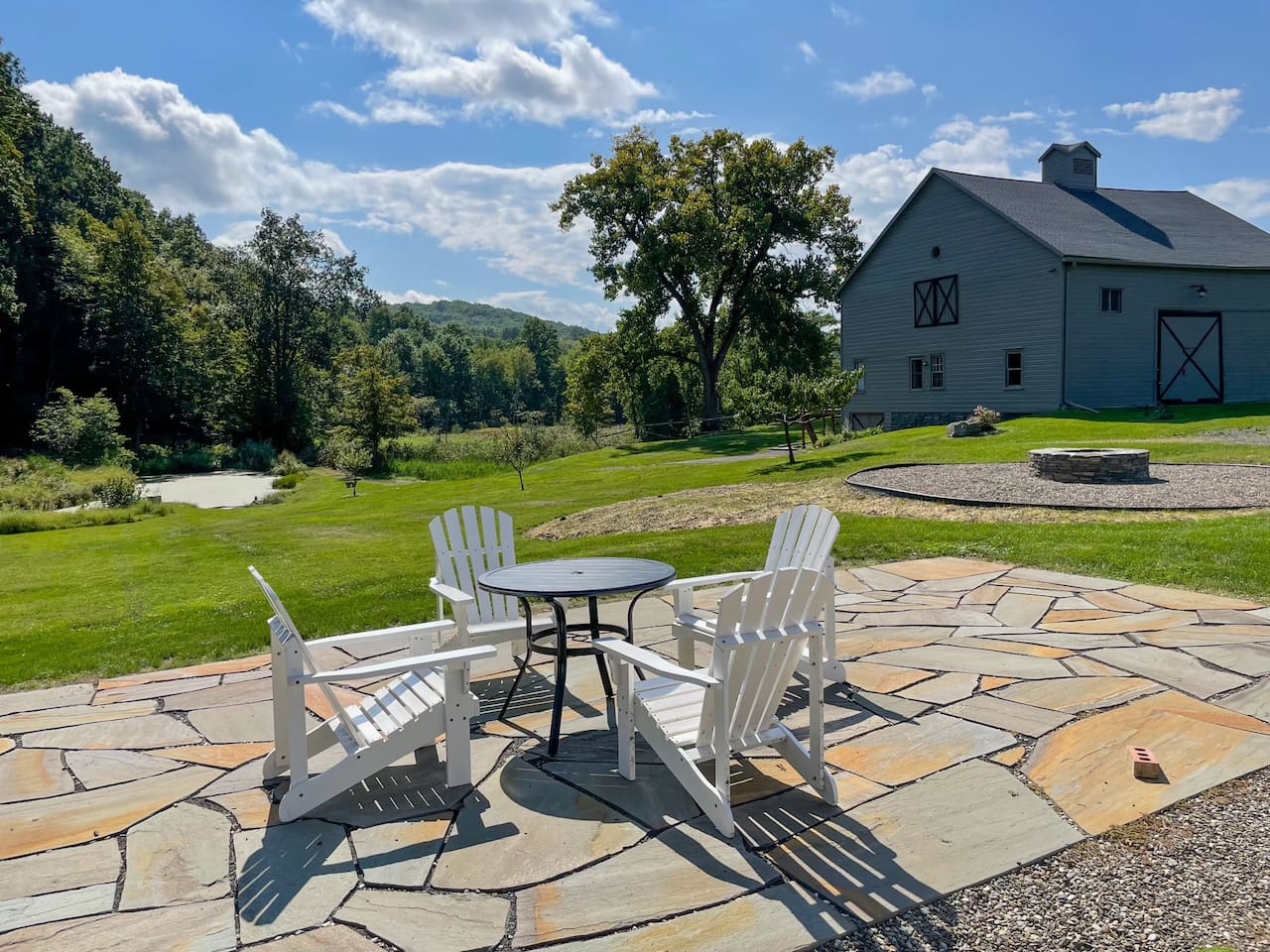 The patio and fire pit sit between the house and barn apartment. The fields slope down towards a pond. Private road access continues up the mountain.
