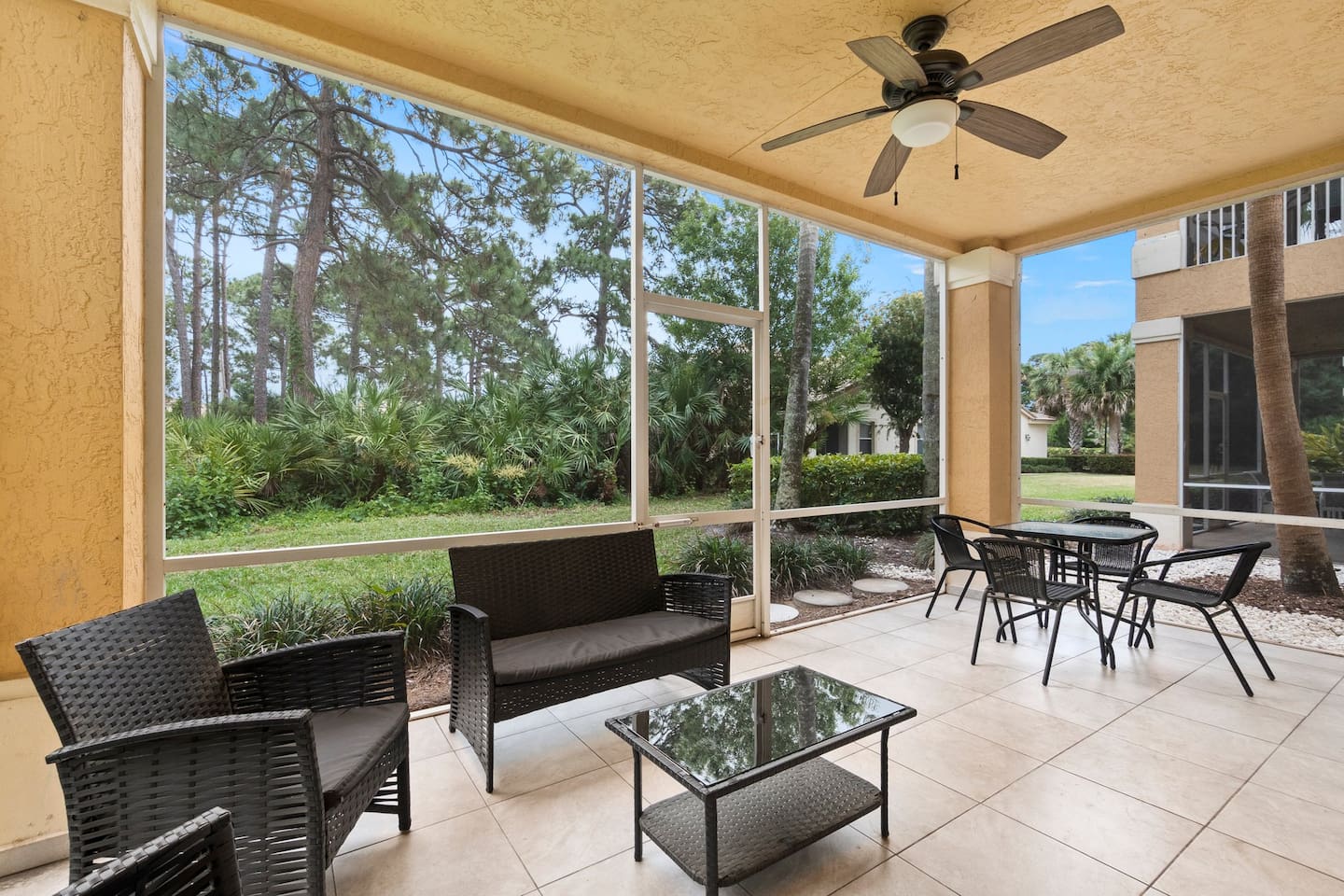 Spacious screened patio with multiple seating areas, ceiling fan, and relaxing garden views.