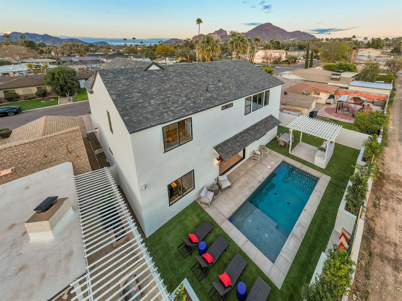 The aerial view of the house captures its luxurious charm, showcasing the private backyard with a crystal-clear heated swimming pool at the center. Surrounding the pool, sun loungers are neatly arranged, perfect for relaxation under the sun.