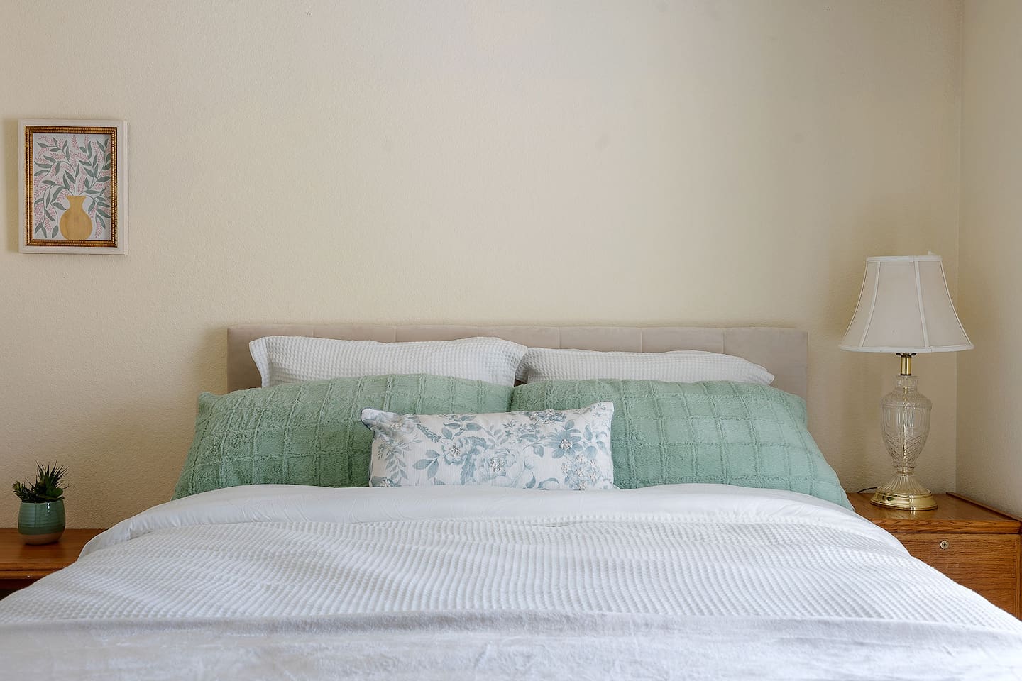 Step into this inviting bedroom featuring a cozy bed, a bedside lamp, and a charming piece of wall art.