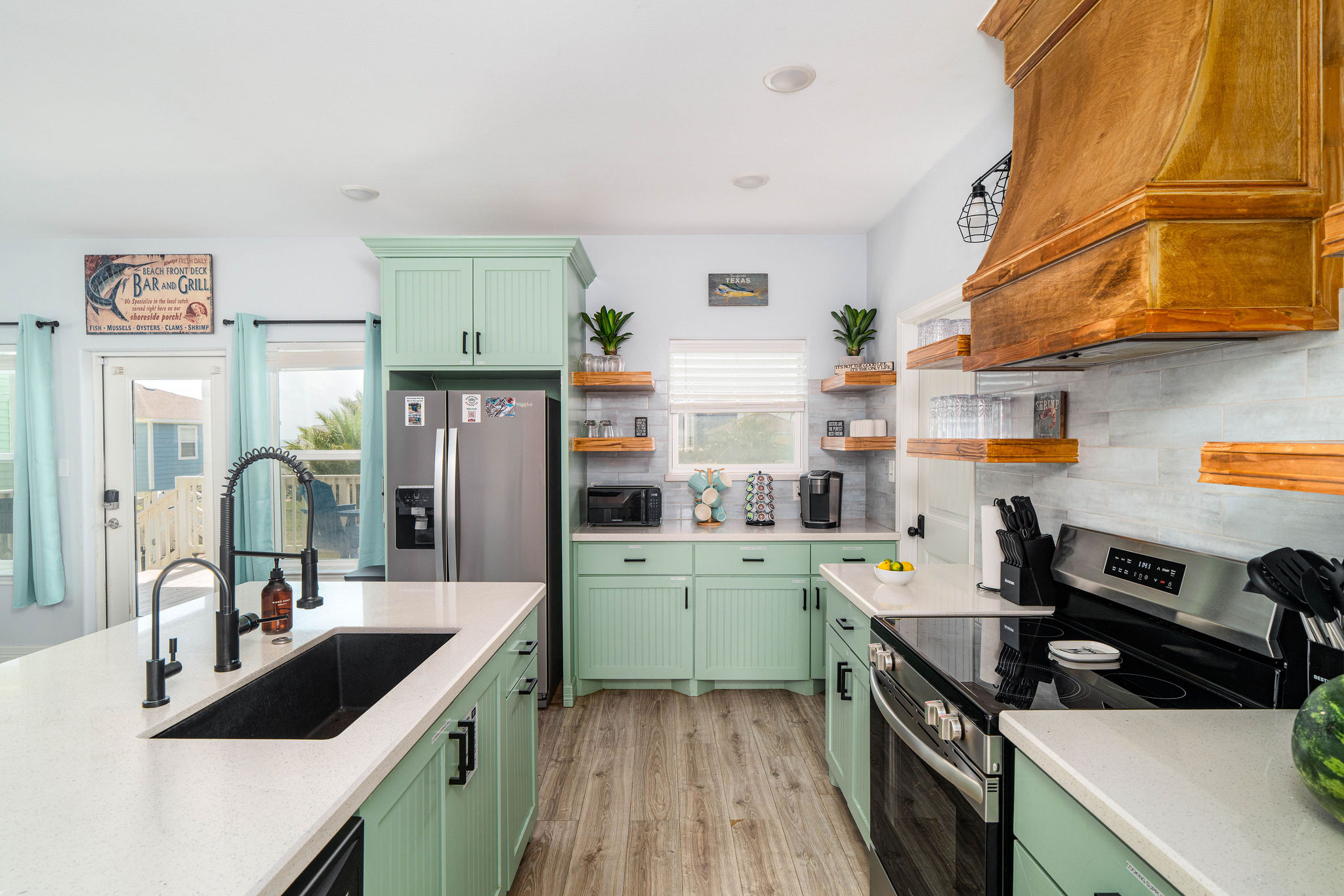 Kitchen detail — coastal green cabinetry, stocked utensils, full-size appliances. Cook like you're home.