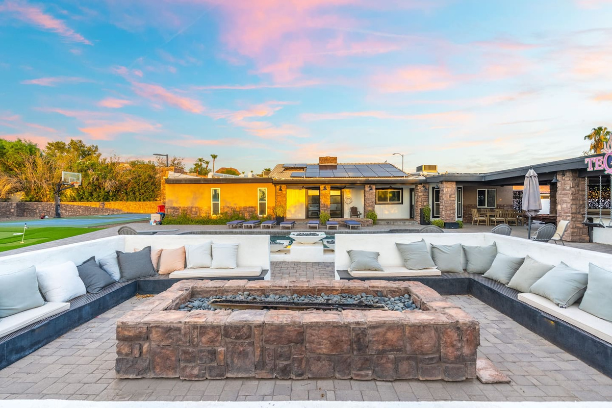 A built-in fire pit lounge with wraparound seating overlooks the pool, putting green, and sport court at dusk.