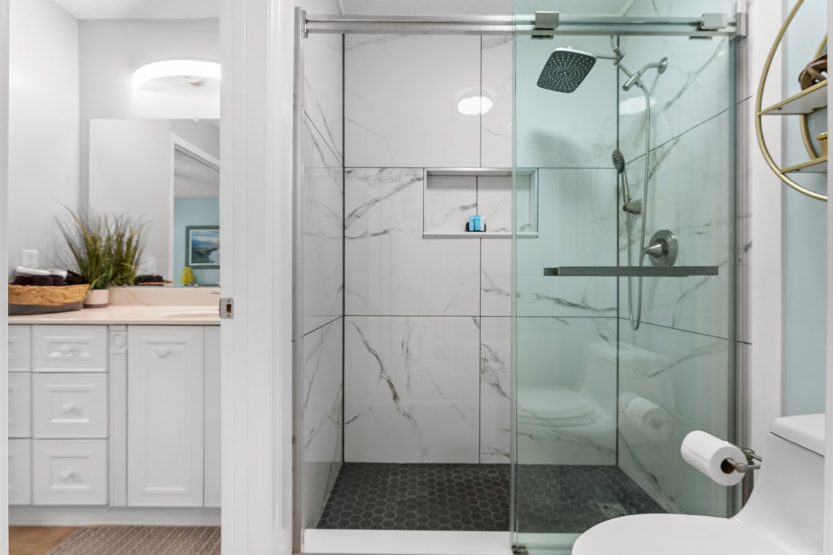 Completely remodeled master shower featuring beautiful tile and a luxurious rain shower head — now conveniently accessible through the hallway half bath.