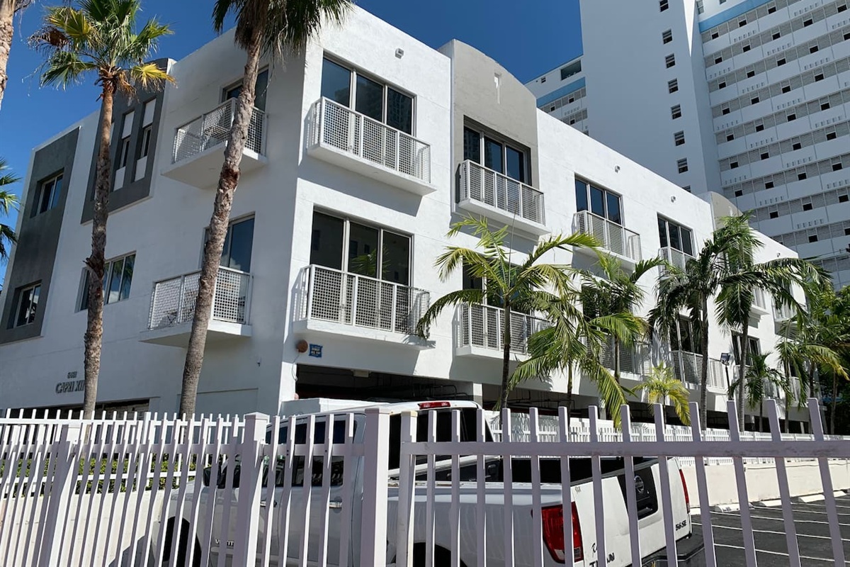 Small townhouse building in classic Miami white with grey accents, framed by palms