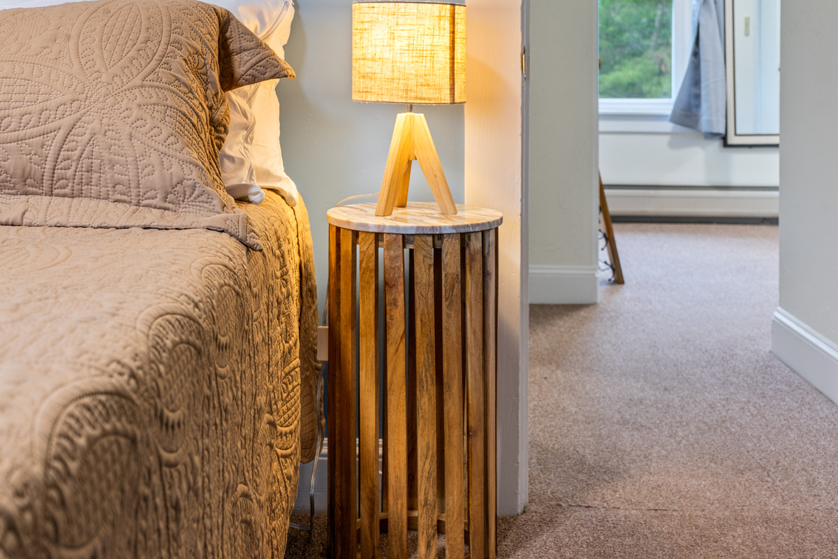 Under the warm glow of the tripod lamp, unique end tables resembling old-style lobster traps bring authentic coastal character to your bedside. The open doorway keeps you connected to the upper landing for an effortless morning routine.