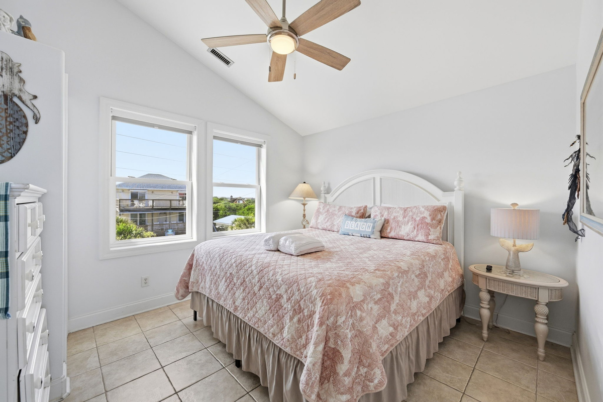 Bright king master bedroom with ocean views, soft coastal d&eacute;cor, and natural light throughout