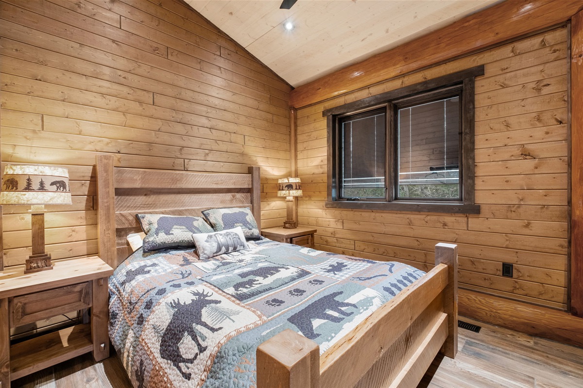 Inviting queen bedroom with rich wood paneling, forest-view window, and custom log furniture — a relaxing retreat after a day on the lake.