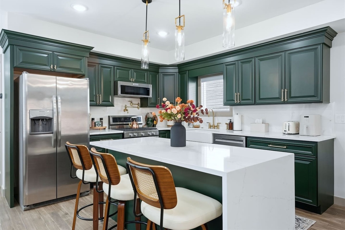 Stylish kitchen with rich green cabinetry, modern lighting, and a spacious island with seating—perfect for cooking, gathering, and enjoying meals together.