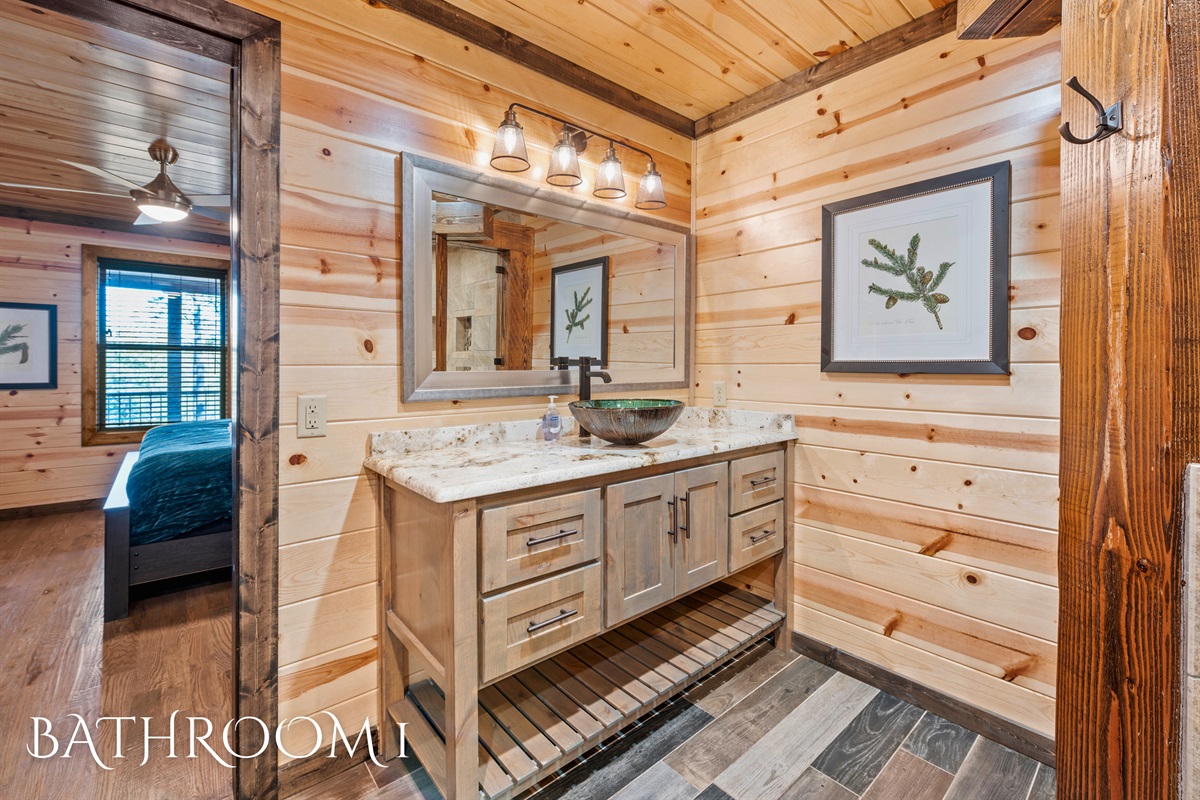 A beautiful bathroom vanity with a countertop and unique vessel sink, set against wood paneling with framed botanical prints