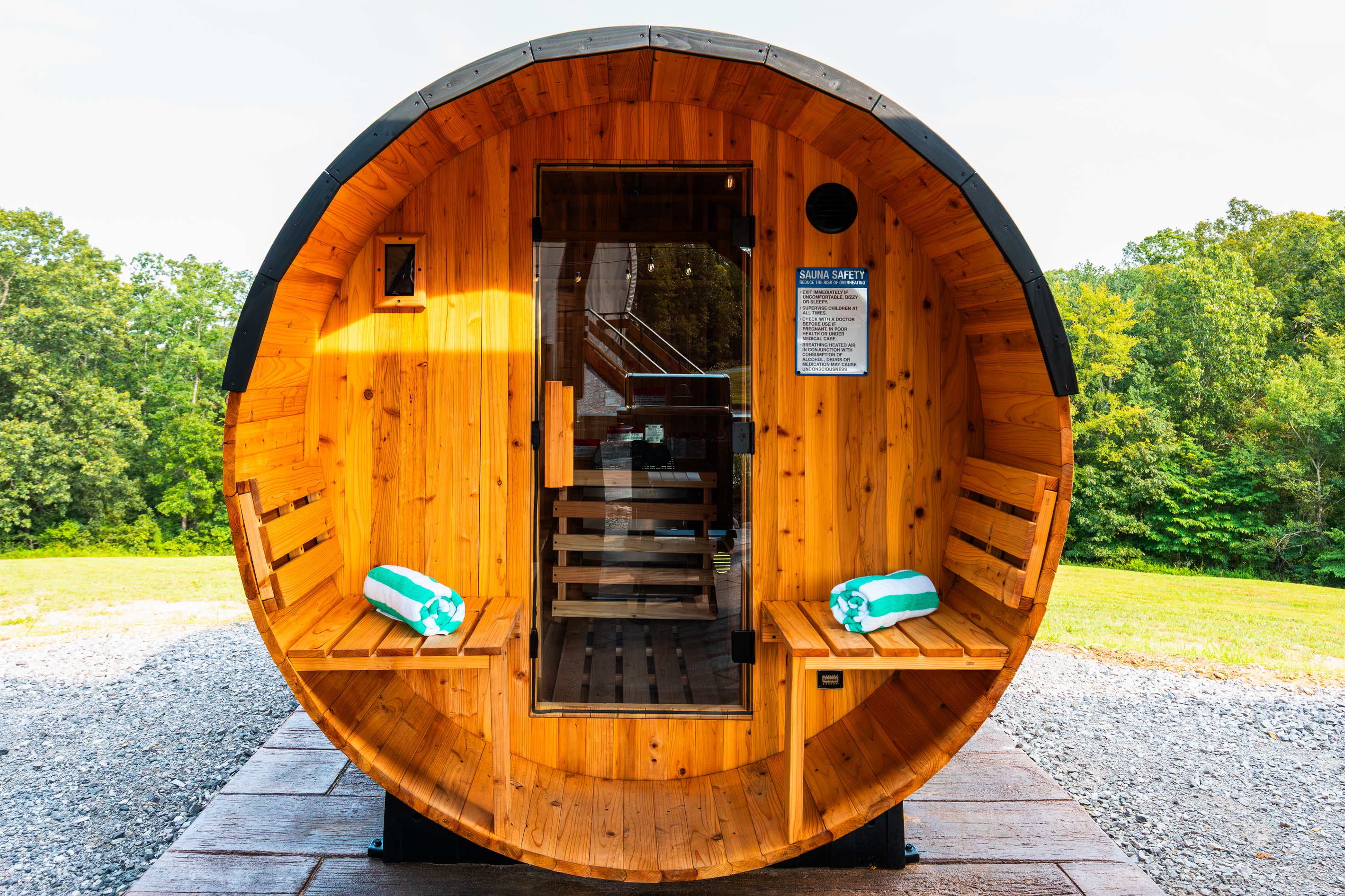 Private barrel sauna with front porch seating, towels, and relaxing wooded views.