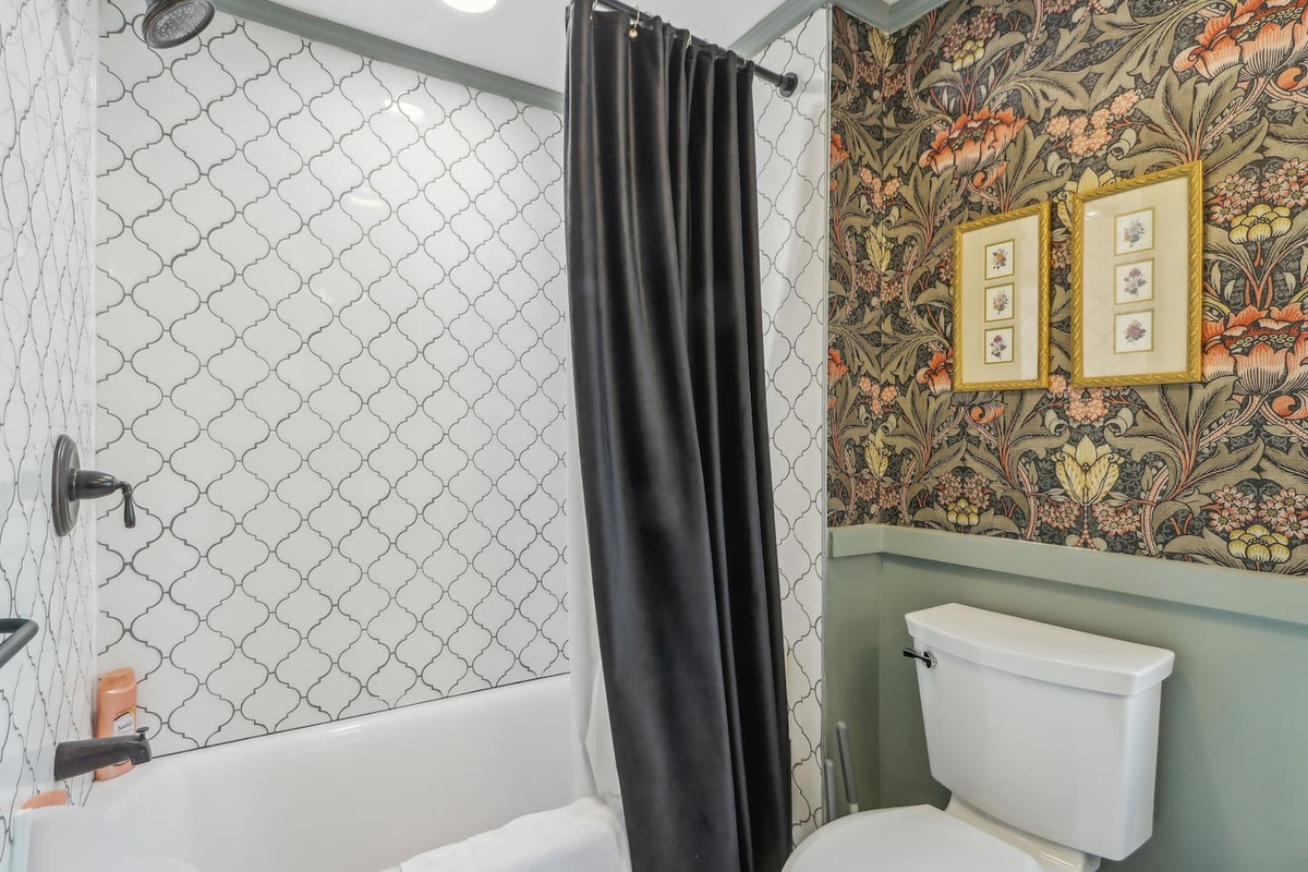 Freshen up in this charming bathroom, complete with a convenient shower/tub combo, patterned tile, botanical wallpaper, and bold accents that add plenty of personality.