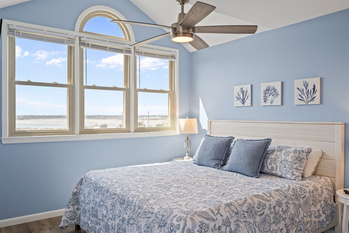 This light-filled bedroom offers expansive windows and a ceiling fan, creating the perfect balance of fresh air, comfort, and calm.