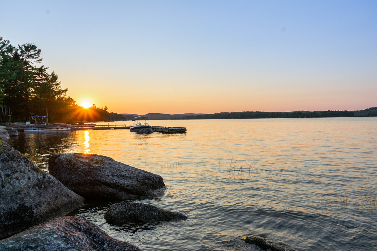 East side view from the beachy water entry at Loonrise Point! Sunburst sets over the neighboring public boat launch and docks across Beech Hill Pond. Easy wade-in shore access makes launching kayaks or paddleboards a breeze in Otis, ME.