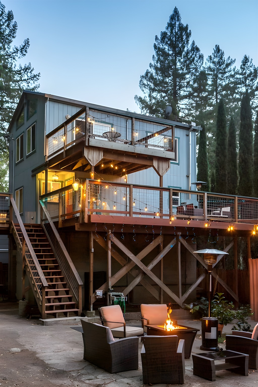 - Elevated two story home with wraparound deck and string lights for charm  
- Outdoor seating with fire pit creates a cozy gathering space at night  
- Surrounded by tall pines for a peaceful and private retreat experience  
