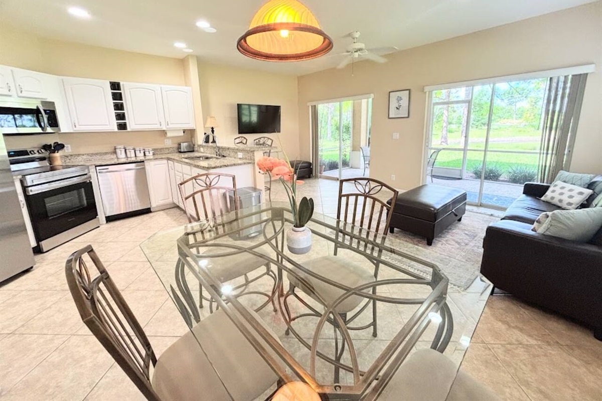 Bright open-concept living and dining area with a fully equipped kitchen, comfortable seating, and sliding glass doors overlooking the greenery.