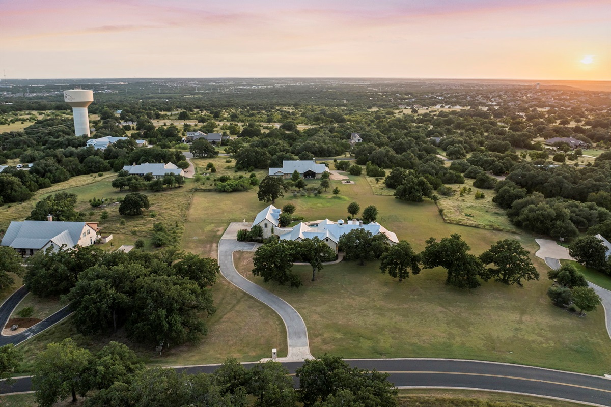 A luxury home surrounded by serene oak trees and rolling green landscapes, bathed in the warm glow of a sunset.