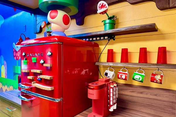 Whimsical kitchen at Mario's Mini Mansion, Clermont, FL! Bright red retro-style fridge, green flooring, yellow walls with Mario shelves, and Toad-inspired decor make post-theme park meal prep an adventure for kids and adults alike.