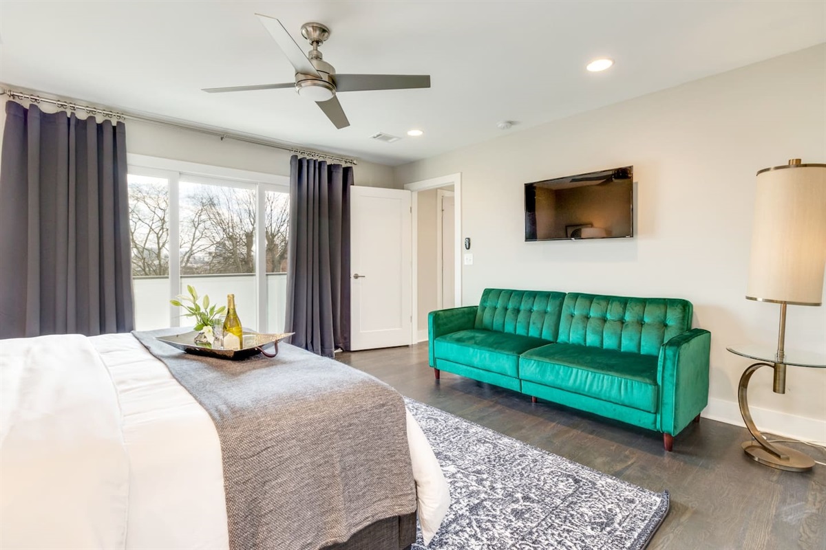 - Emerald green tufted sofa adds a vibrant pop of color to this spacious bedroom lounge - Wall mounted TV and large windows make this a great spot for relaxing or streaming - Sophisticated black out drapes and detailed rug complete the room’s upscale feel