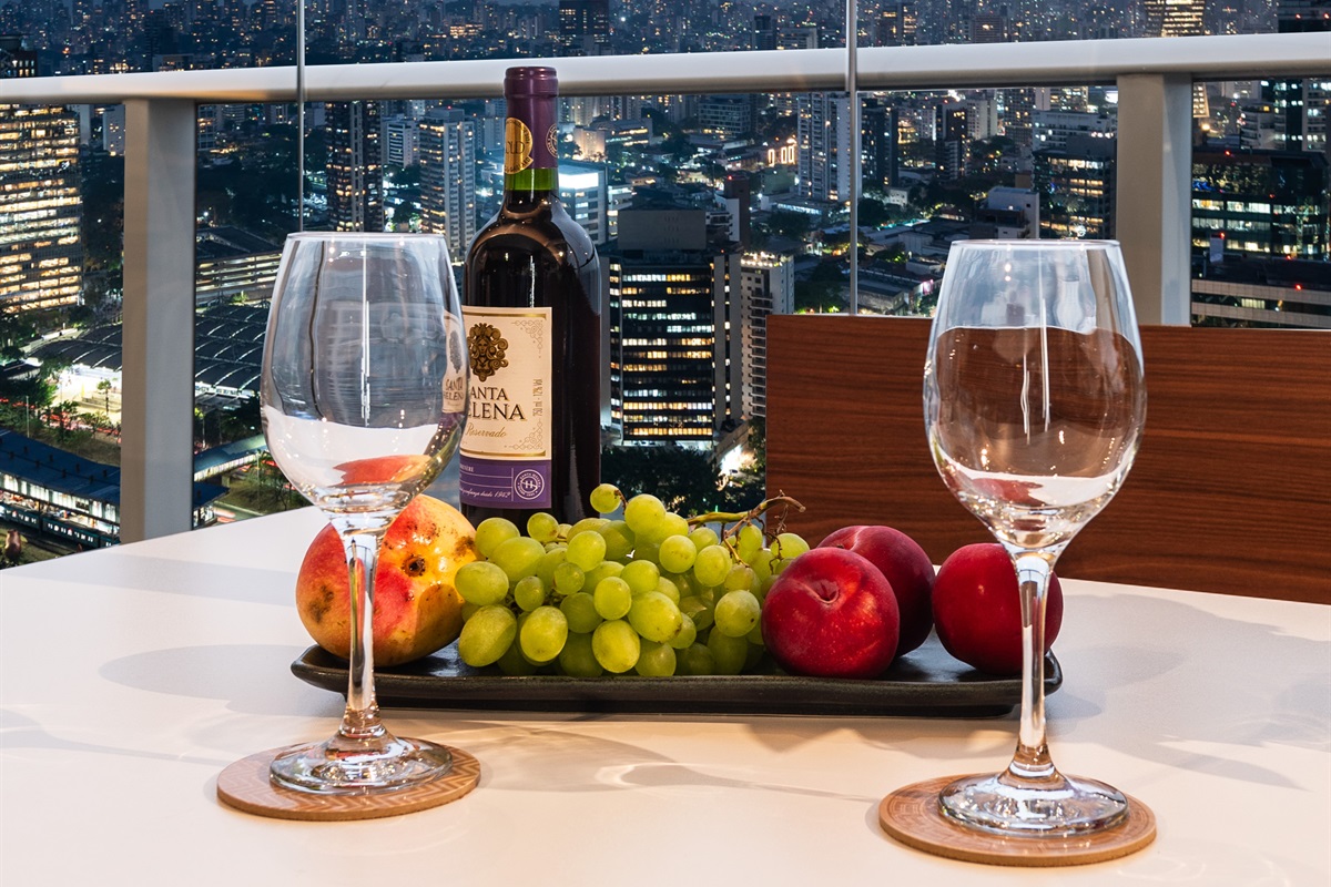 Detalhe lifestyle 🍷 Experiência única: vinho e frutas à mesa com a vista noturna da cidade. Ambiente sofisticado que combina conforto e elegância no River One.