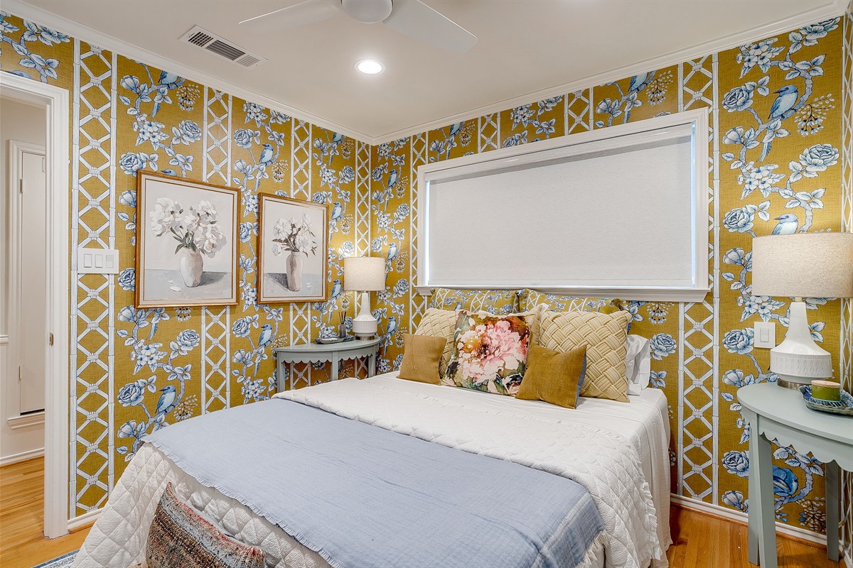 BR4 featuring a cozy queen bed, natural light from surrounding windows, and wallpapered walls that keep the personality flowing throughout the home.