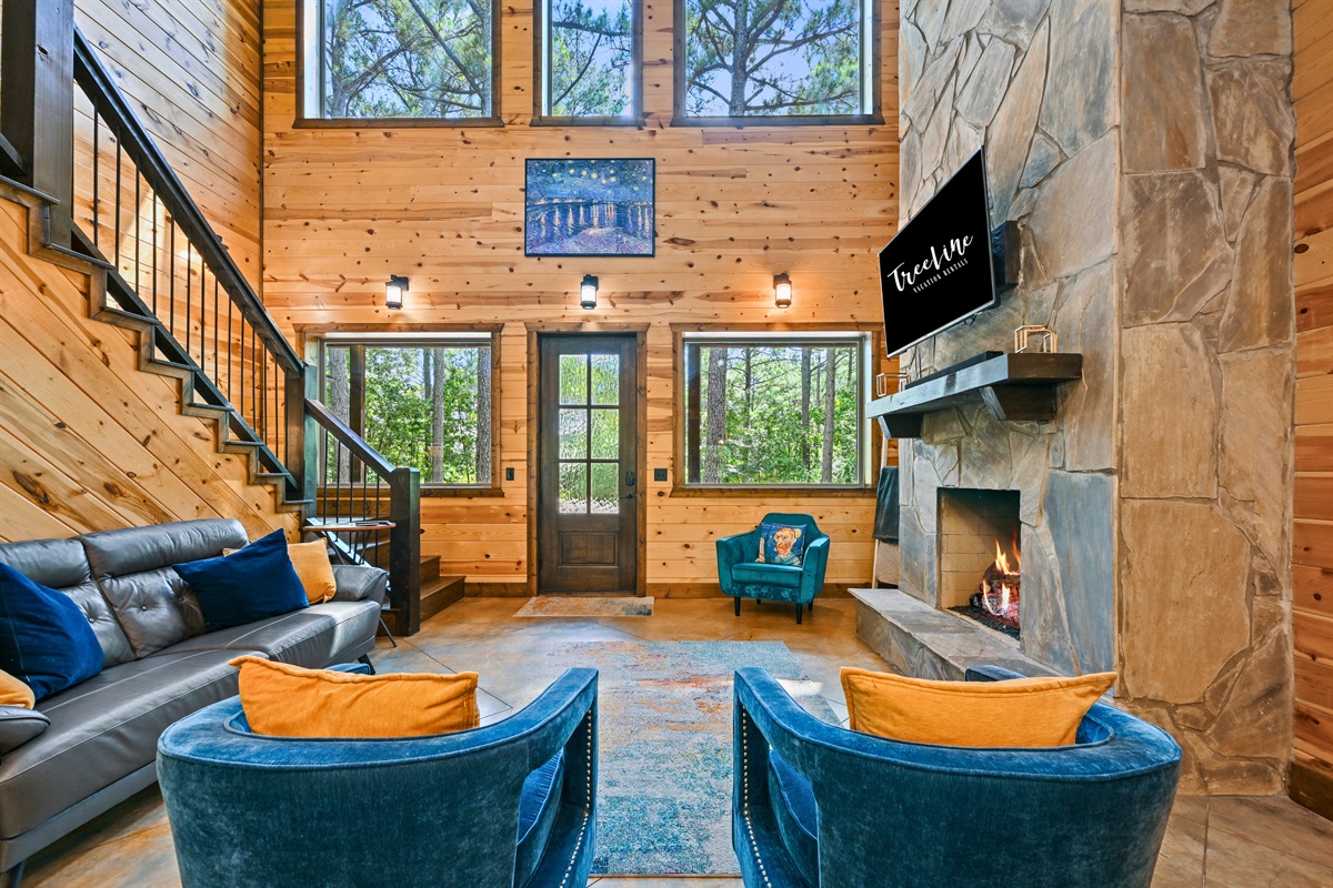 The open-concept living room features soaring ceilings, cozy seating, and a stone fireplace that sets the mood for peaceful evenings in.