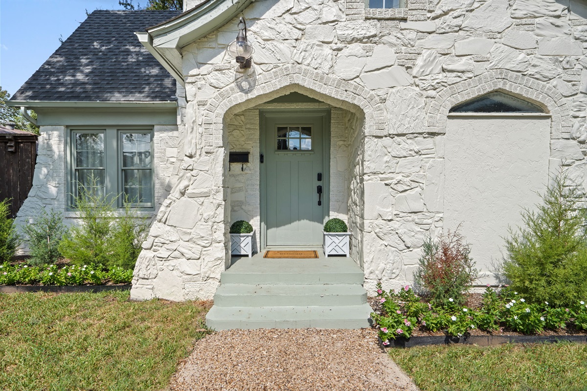 Sage green front entry door set into original 1929 stonework. Covered entry with lush surrounding landscaping and classic Dallas architectural character. Welcome home!