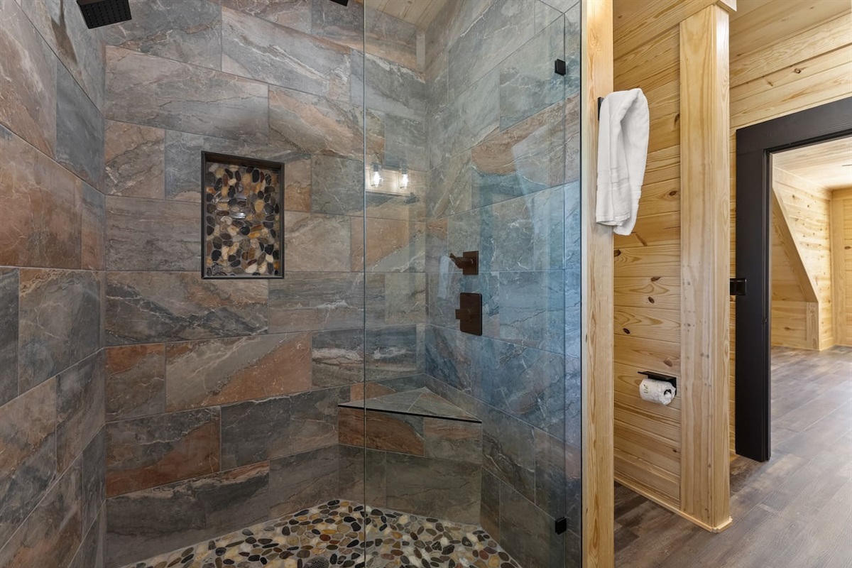 Luxurious walk-in shower with rain showerhead, pebble stone flooring, and built-in bench—your private spa retreat in the mountains
