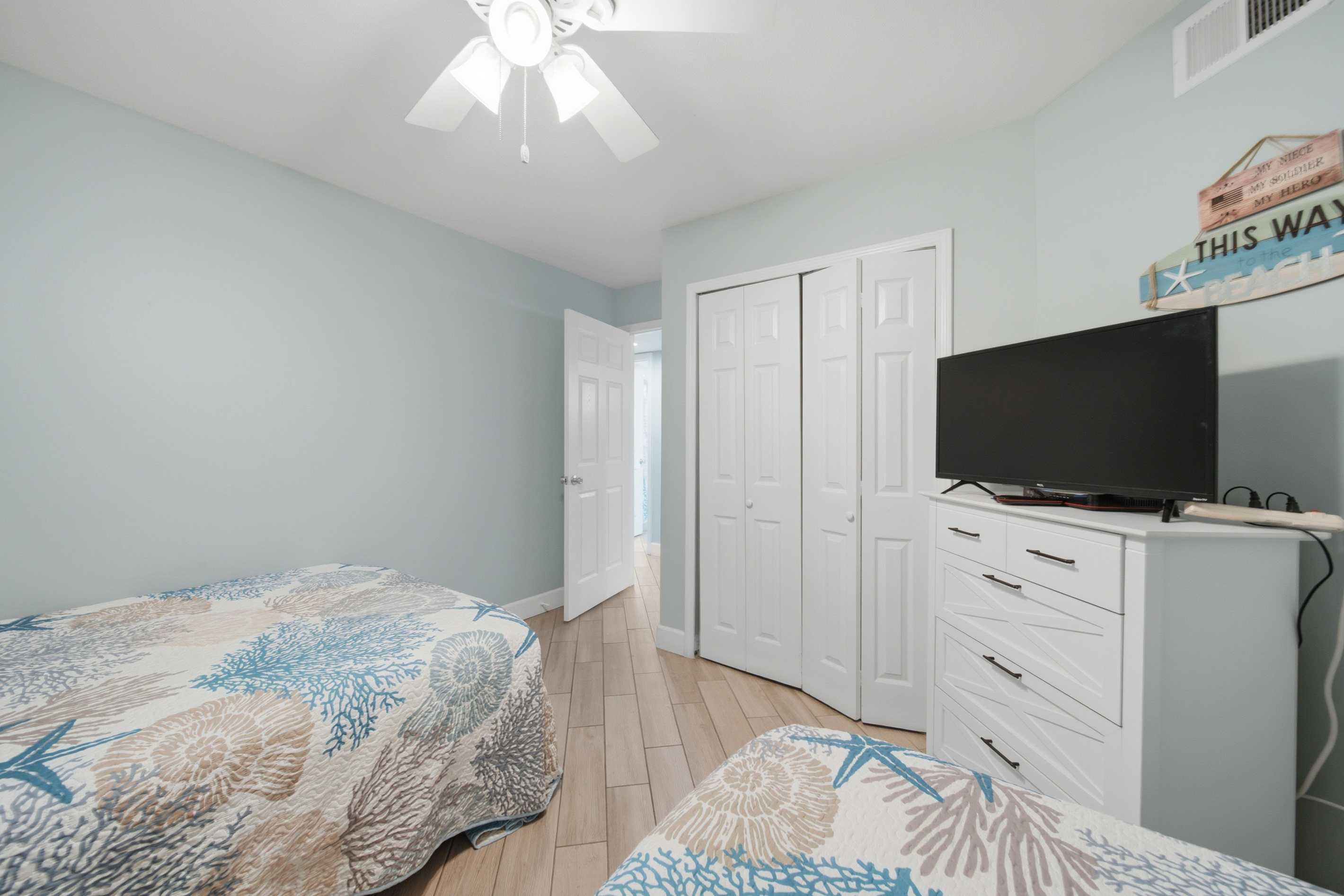 Bright bedroom with plush coastal bedding, ceiling fan, and mounted TV