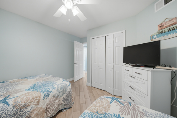 Bright bedroom with plush coastal bedding, ceiling fan, and mounted TV