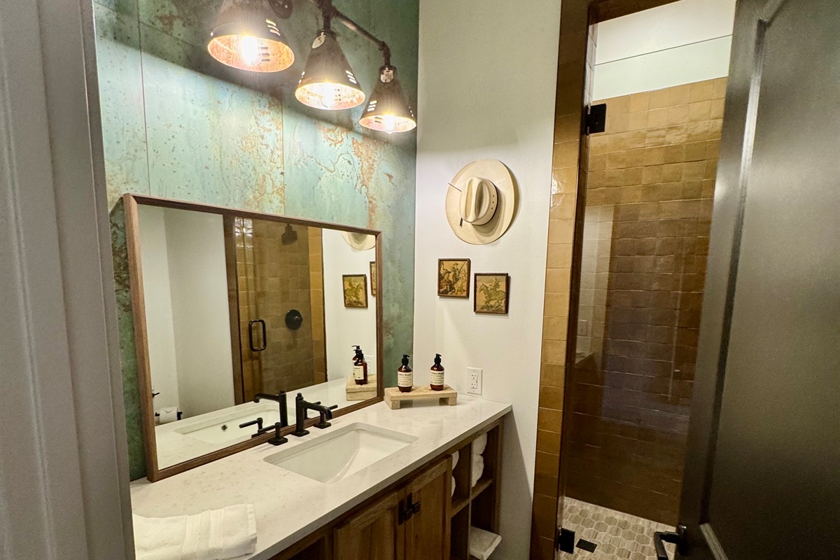Private en-suite bathroom at the Corral Suite — a designer vanity, framed art, and modern Western finishes throughout.
