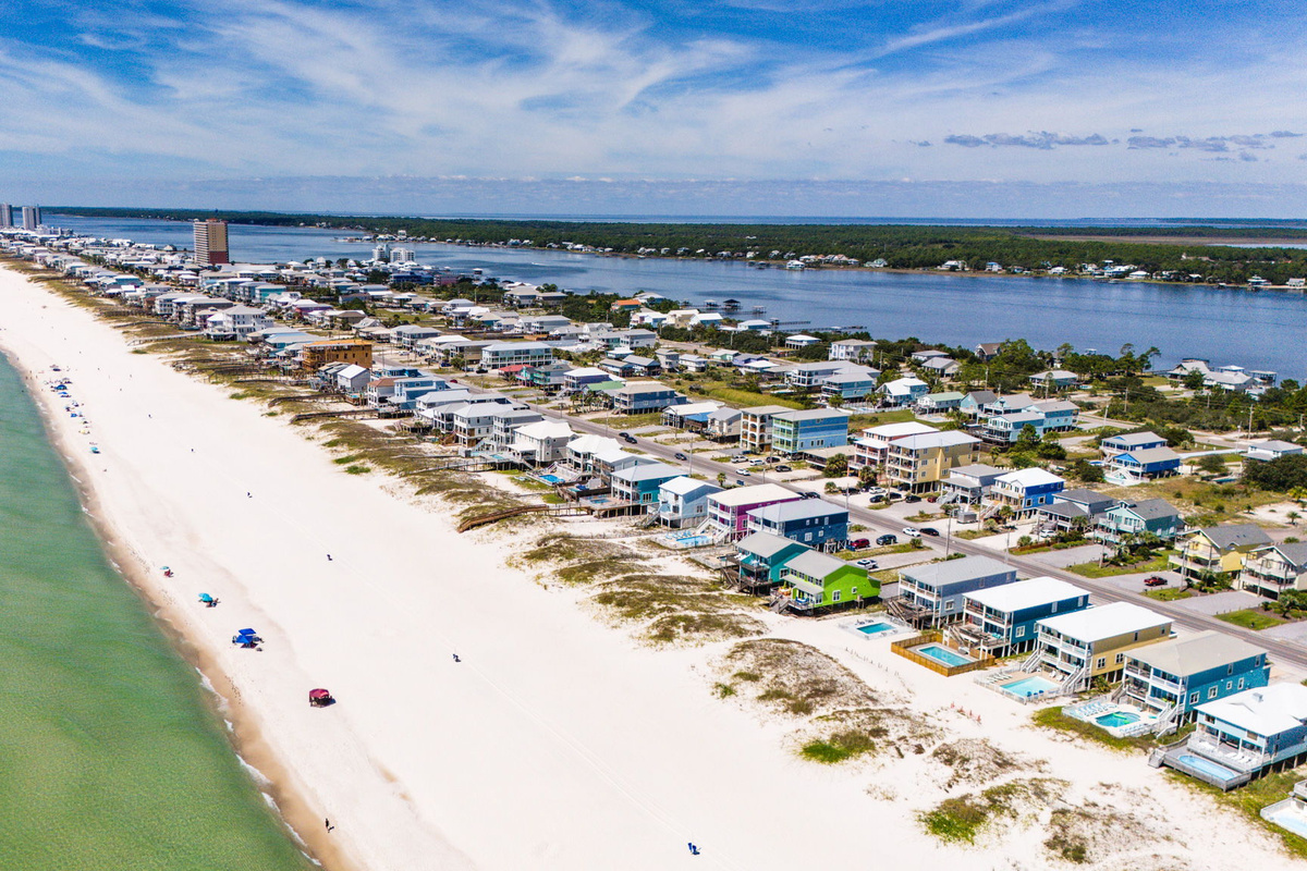 Panoramic aerial view of the Gulf Coast beach, highlighting the wide sandy shoreline, blue water, and nearby vacation homes.