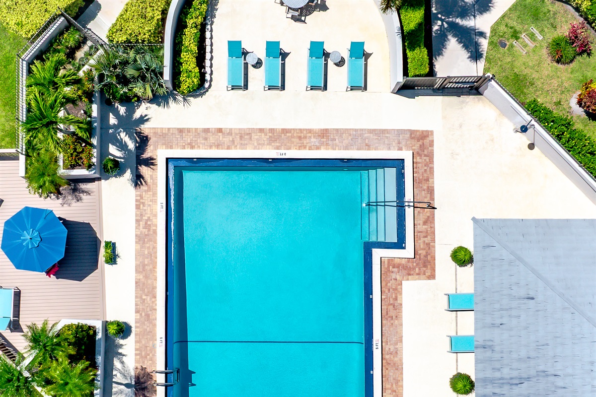 Resort-style heated community pool surrounded by lush tropical landscaping, sun loungers, and peaceful lake views — perfect for relaxing after a day at the beach or golf course.
