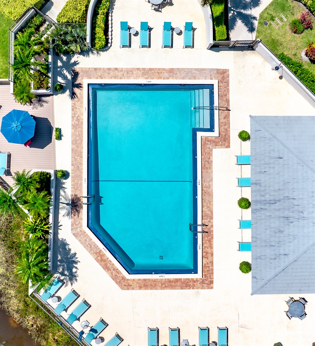 Resort-style heated community pool surrounded by lush tropical landscaping, sun loungers, and peaceful lake views — perfect for relaxing after a day at the beach or golf course.
