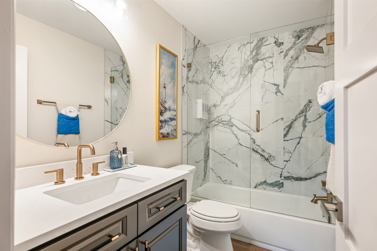 Modern full bathroom with marble-style shower and sleek vanity finishes.