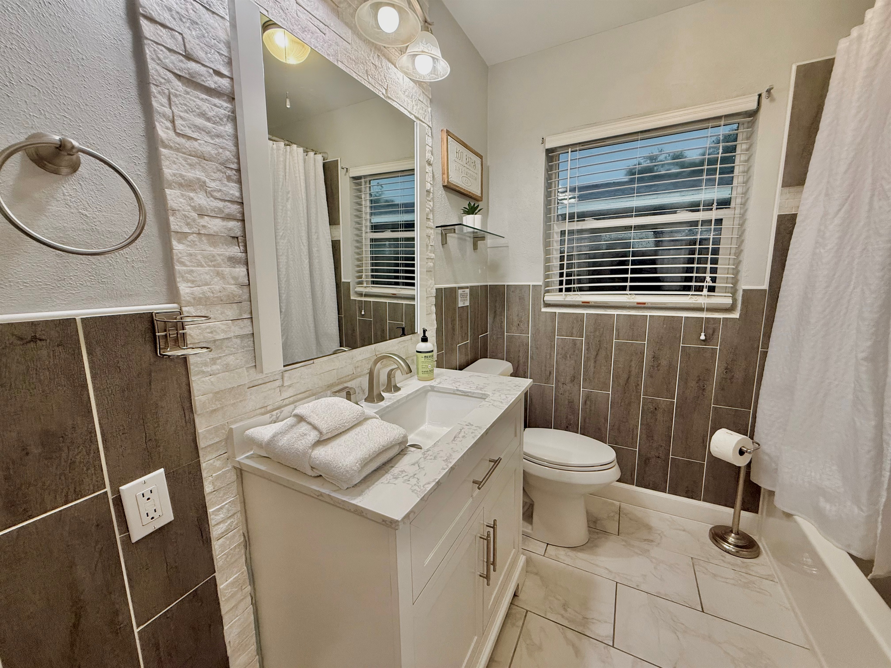 This freshly updated bathroom boasts chic tile design, a bright vanity with marble top, and a deep soaking tub with shower.