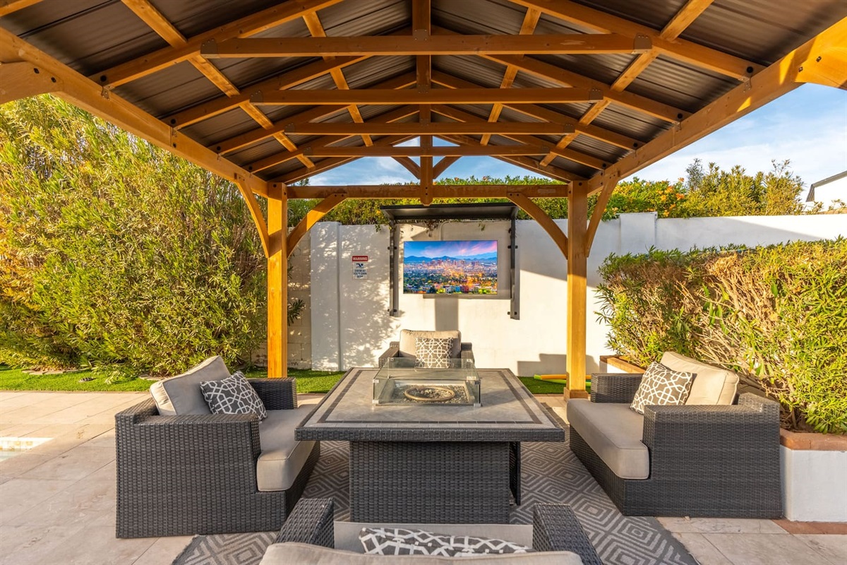 This stylish wood gazebo includes a TV and plush outdoor seating around a fire table—your private open-air cinema and lounge.