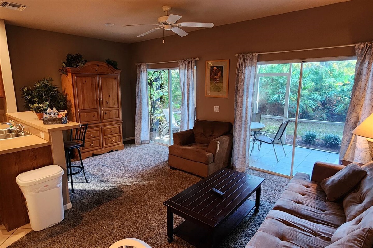 Spacious living area with comfortable seating, large windows, and sliding glass doors leading to the private screened patio.