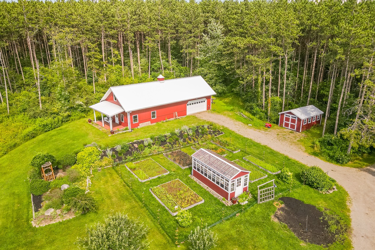 Charming country living with a classic red barn, greenhouse, and lush garden beds surrounded by nature’s beauty.