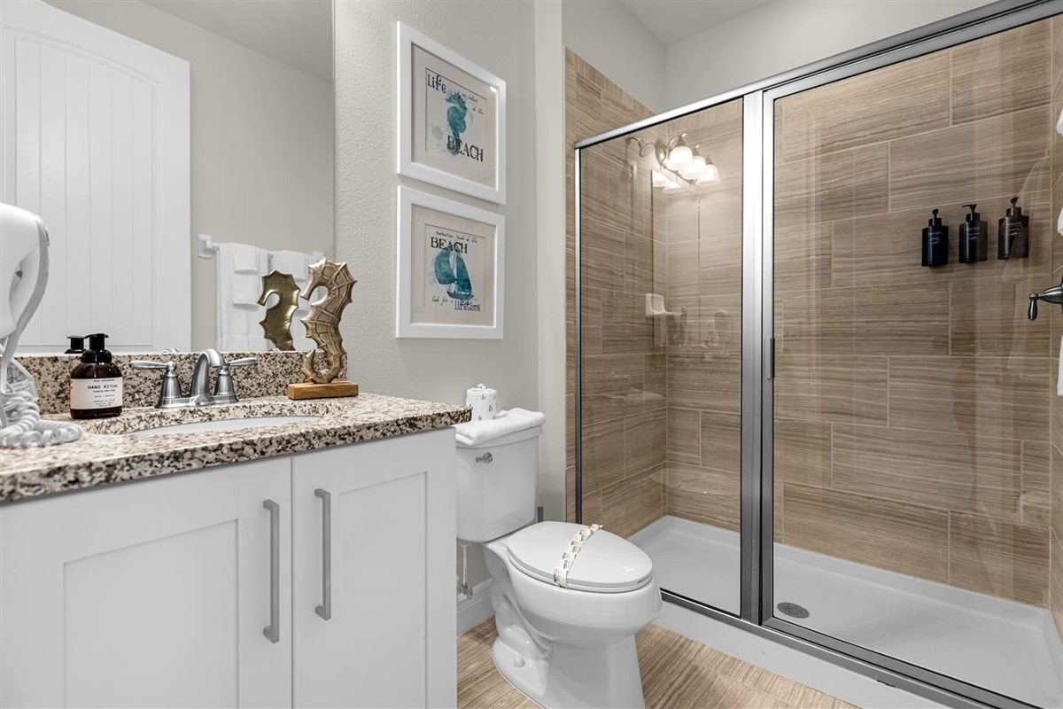 Spacious full bathroom featuring a glass-enclosed shower with elegant wall design, a sleek toilet, decorative frame, and a stylish vanity with cabinet storage under the sink. A blend of modern fixtures and tasteful decor create a serene.