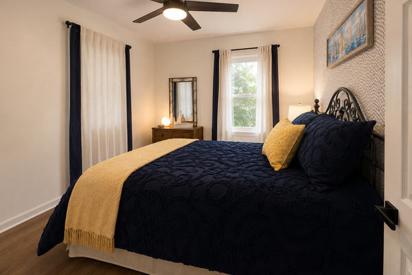 Cozy main-floor bedroom with a queen bed, soft natural light and easy access to the nearby hallway bath.