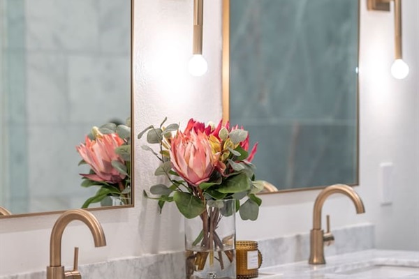 Private ensuite bathroom featuring dual vanities, marble countertops, warm brass fixtures, and a spa-style walk-in shower with floor-to-ceiling stone tile and glass enclosure for a hotel-quality, comfortable experience.