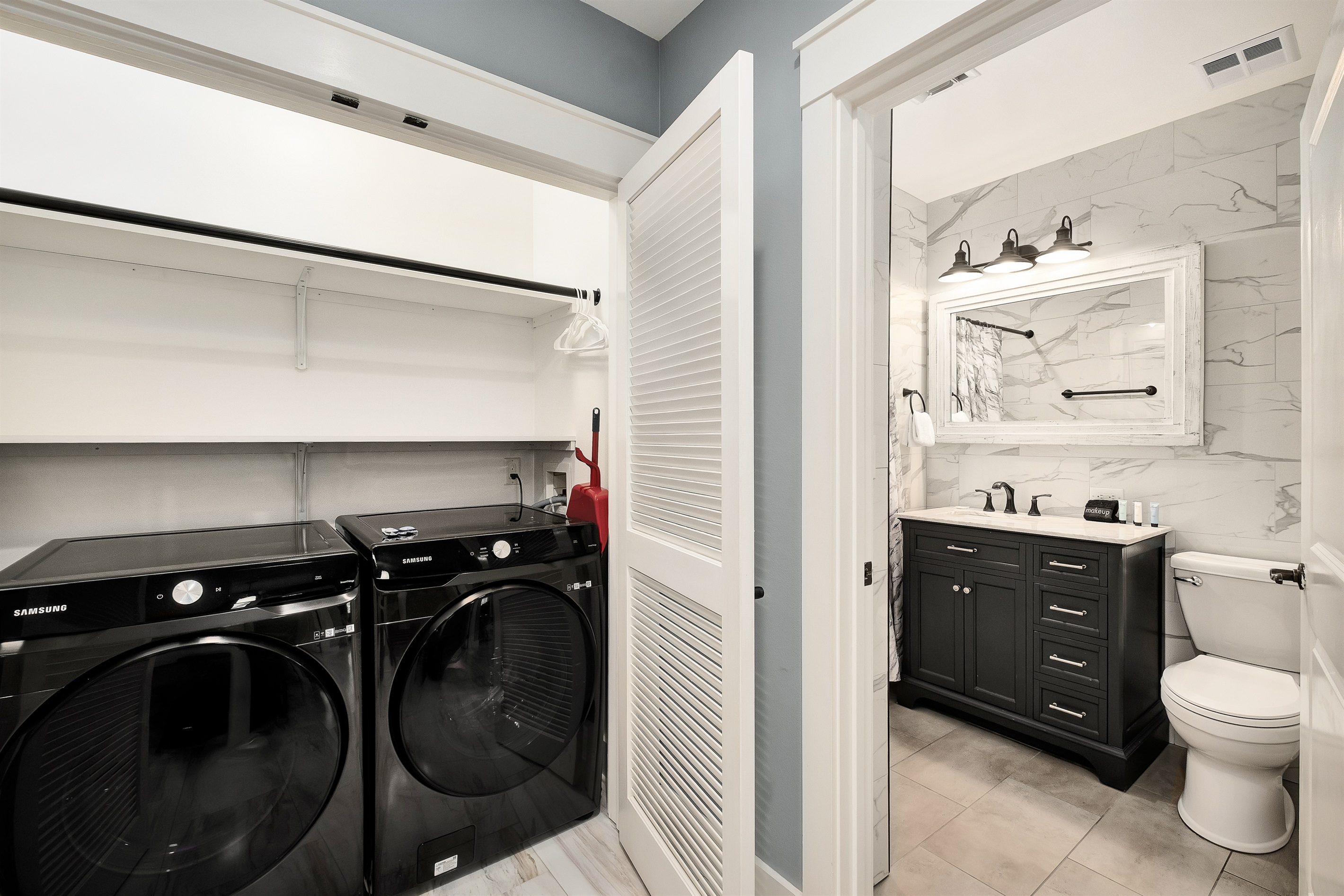 Convenience at your fingertips with in-unit Samsung washer and dryer, located just steps away from a beautifully tiled bathroom featuring modern fixtures and a sleek vanity.